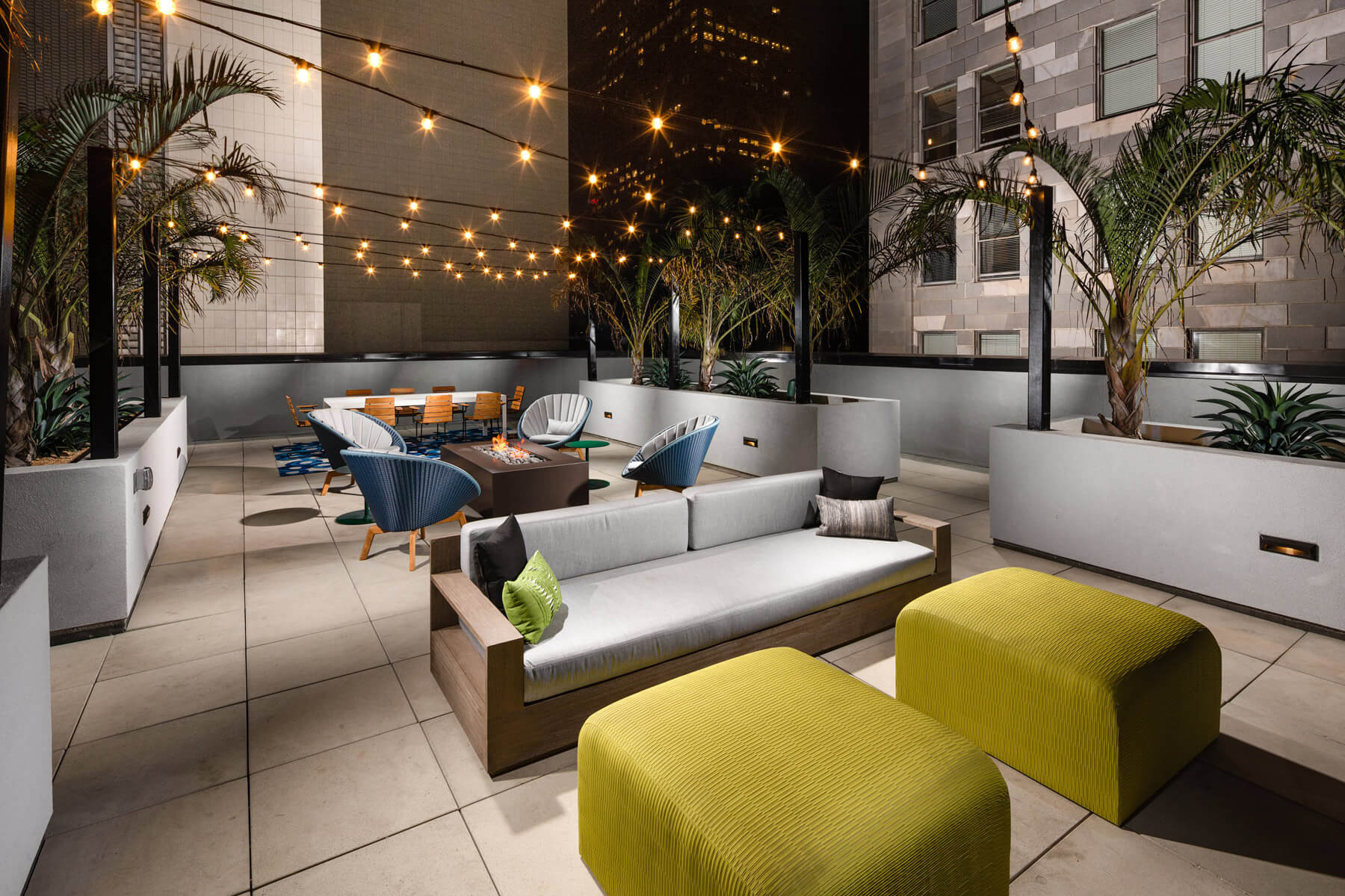 Apartments for Rent in Downtown Los Angeles CA - Beautiful Rooftop Lounge With String Lighting, Firepit Surrounded by Plush Outdoor Seating, and Gorgeous View of Los Angeles Skyline.